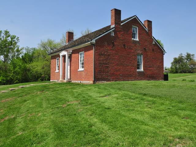 The exterior of a modest red-brick home set against a blue sky.