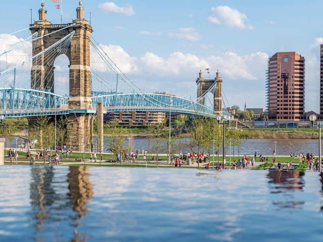 The blue Roebling Suspension Bridge spans the Ohio River in springtime with views of Smale Park