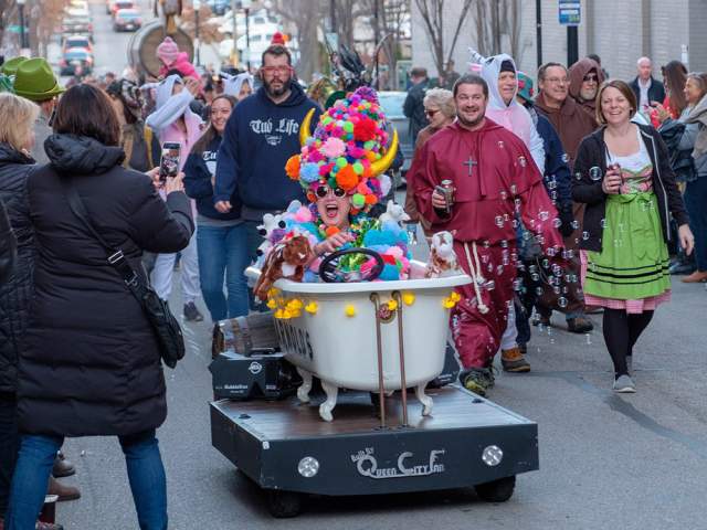 A woman sits in a bathtub during the Bockfest parade wearing a colorful pompom hat
