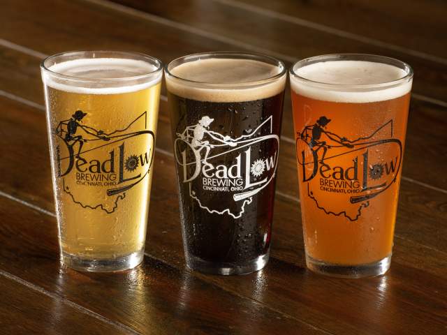 A trio of pint glasses sit on a wooden bar. From left to right they are a pale beer, dark beer, and amber colored beer.