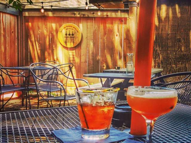A wooden patio with sunshine and two peach-colored cocktails on an iron table