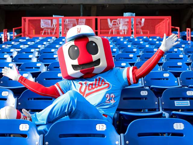 An anthropomorphic version of the famous red and white striped Florence, KY watertower, dressed in a blue and red Florence Y'alls uniform. It sits in the stadium seats arms stretched wide.