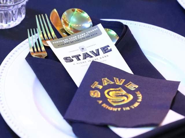 A black, white, and gold place setting. In gold on the black napkin it says 'STAVE: A Night in the Dark'