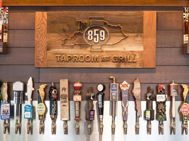 A wall of taps sit below a wooden sign that says 859 Taproom and Grill