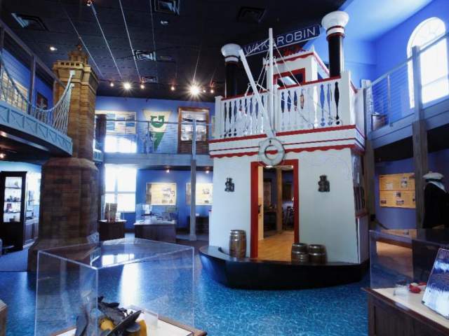 A recreation of a riverboat on a blue floor to represent the Ohio River. A model of the Roebling Bridge sits to the left.
