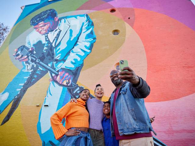 A family takes a selfie in front of the Mr. Dynamite James Brown mural in OTR