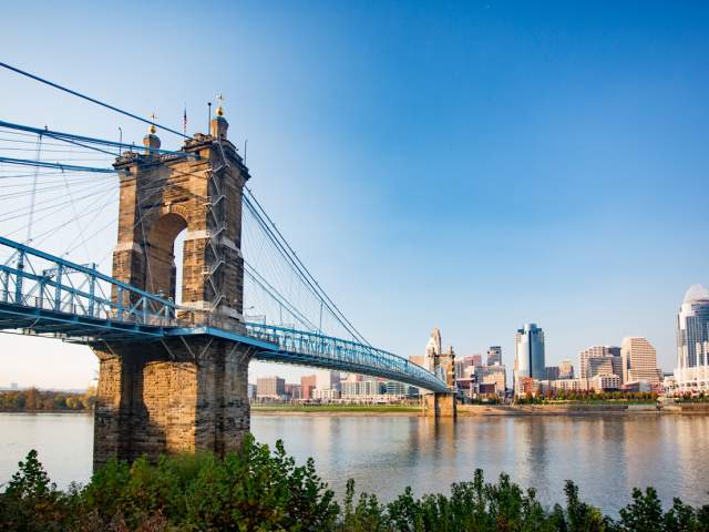 The Roebling Suspension bridge leading to downtown Cincinnati's skyline under a sunny blue sky