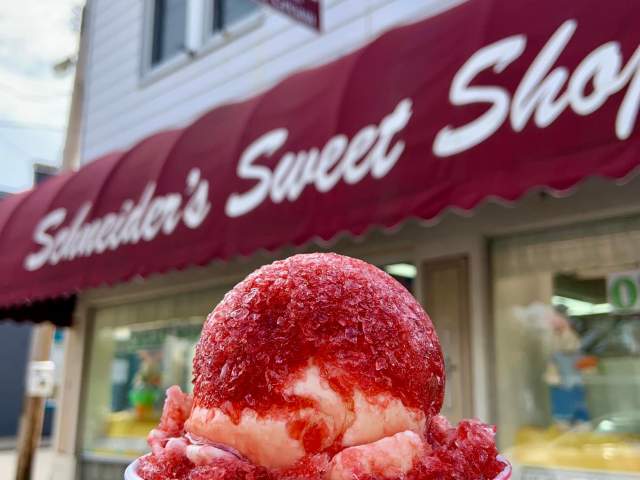 An ice ball, a snow cone and ice cream hybrid, in front of the red and white Schneider's Sweet Shop awning.