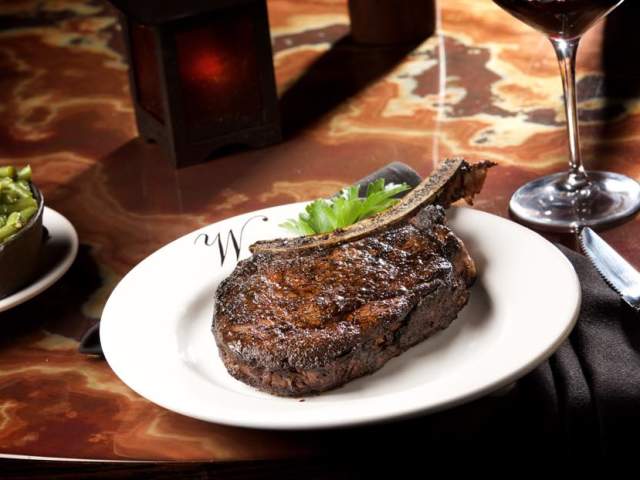 A bone-in ribeye sits on a white plate.