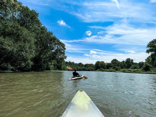 A view of the Little Miami River, and a person in a kayak, from another person sitting in a kayak.