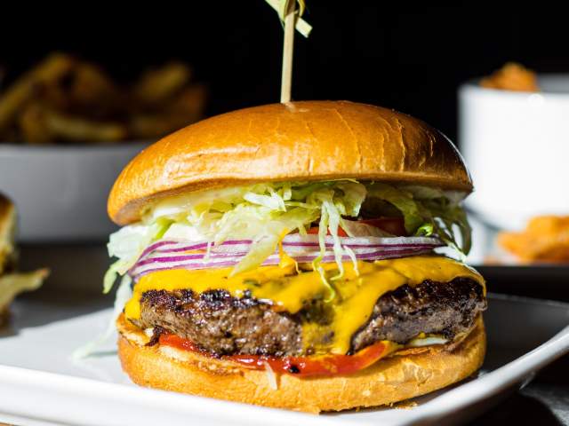 A classic cheeseburger on a bun with lettuce, red onion, and tomato. A pick goes through the bun holding it together.