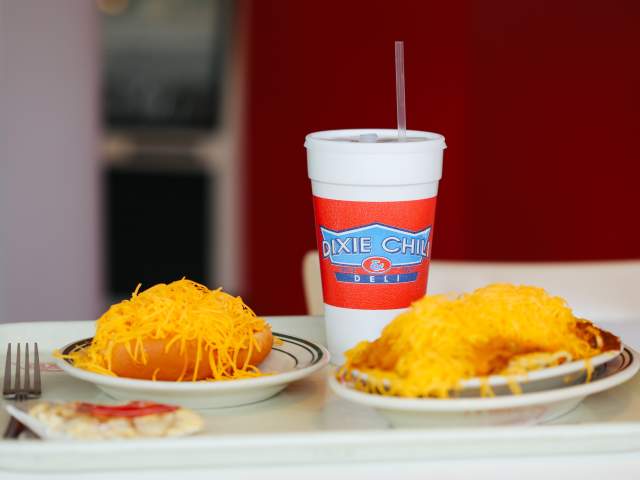 A cheese coney and chili spaghetti piled high with cheese, and drink sit on a tray from Dixie Chili