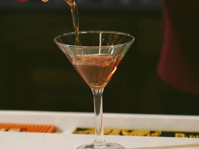 A cocktail is poured into a glass from a strainer.