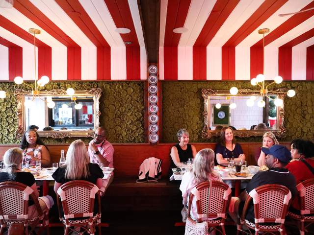 A group of people sit a tables under a red and white striped ceiling.