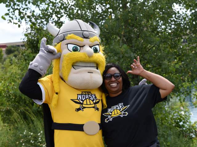 A viking mascot and student stand side by side with their hands making the NKU sign for a horned helmet.