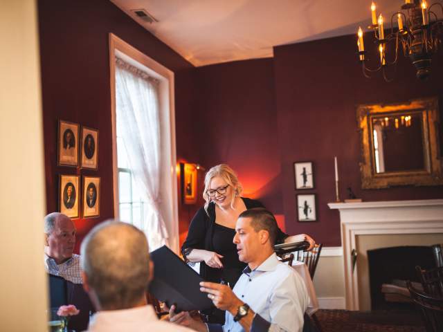 A smiling server attends to a group of diners in a room painted burgundy.