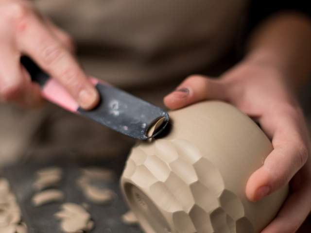 Close up of a person carving a design into a piece of pottery.