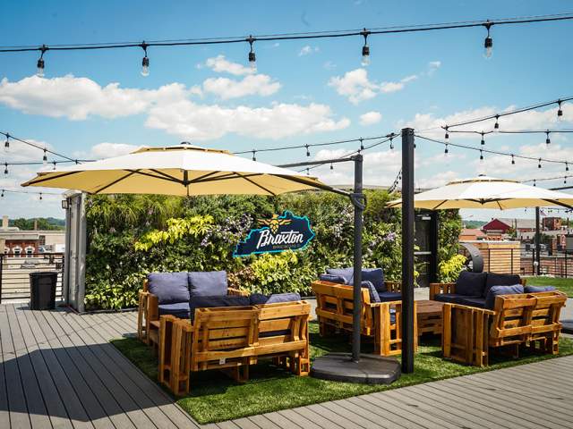 A patio set, umbrellas and string lights sits on a rooftop deck in front of a living plant wall that says Braxton