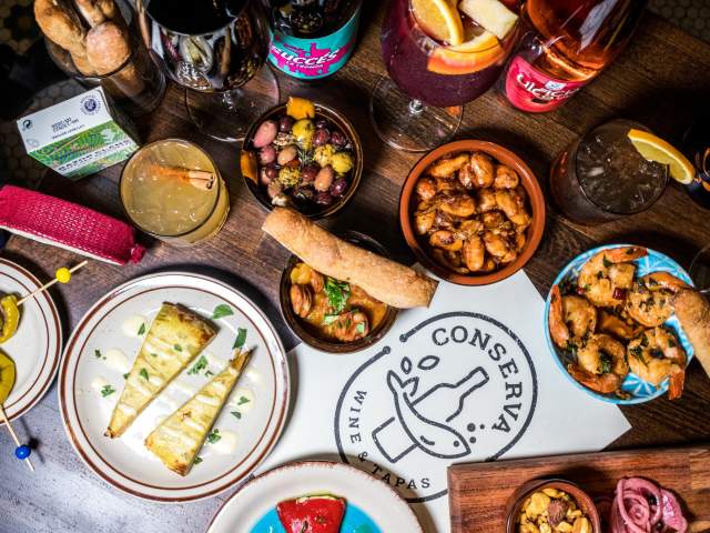The image is an ariel view of different foods and drinks on a table with a Conserva logo sign.