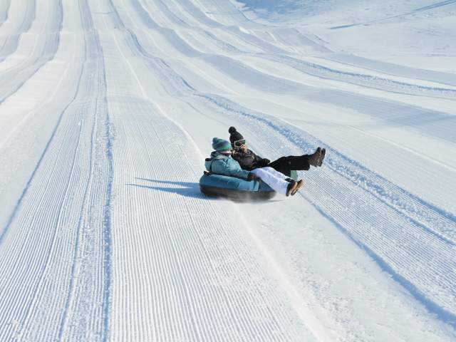 Image is on two people sharing a black inner tube sliding down a hill covered in snow.