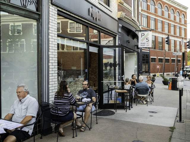 A group of people sits at black metal patio tables on a sidewalk outside Ripple Wine Bar