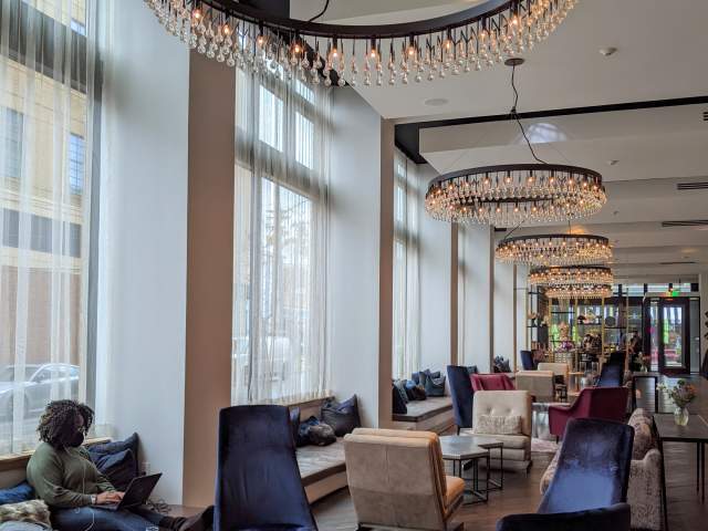 A woman working on laptop in the spacious lobby of Hotel Covington with four round chandeliers hanging overhead