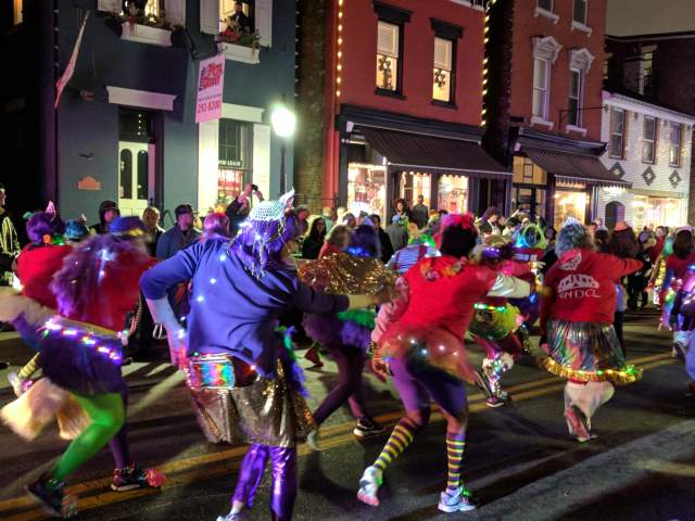 People in bright colors wearing light up shoes and other lights in the Mainstrasse Village Mardi Gras parade