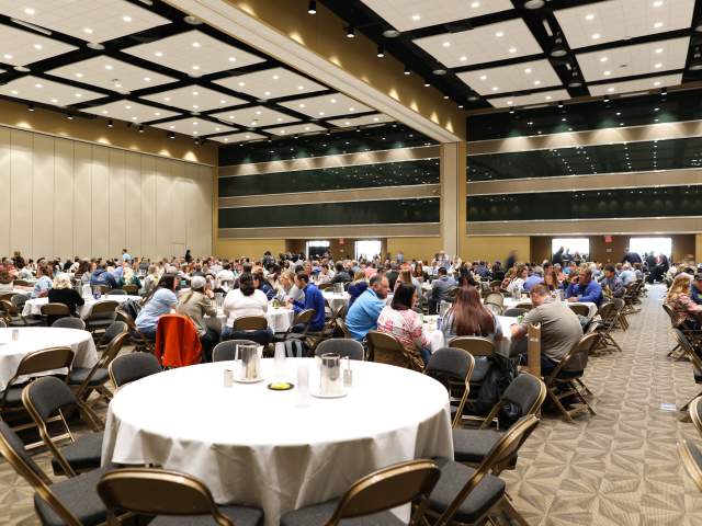 Attendees gather around circular tables in a large banquet room.