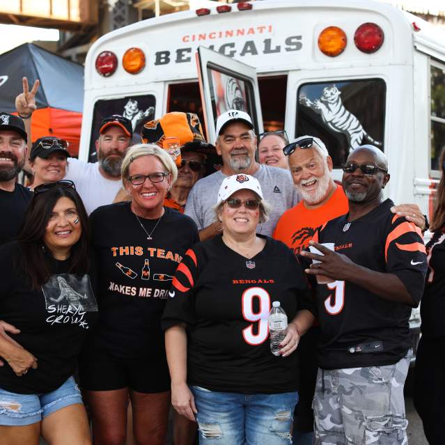 A group of 12 Bengals fans decked out in gear pose in front of a Bengals bus.