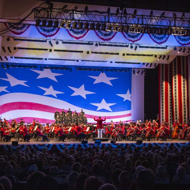 The Cincinnati Symphony Orchestra performs onstage with American flag decor as a backdrop