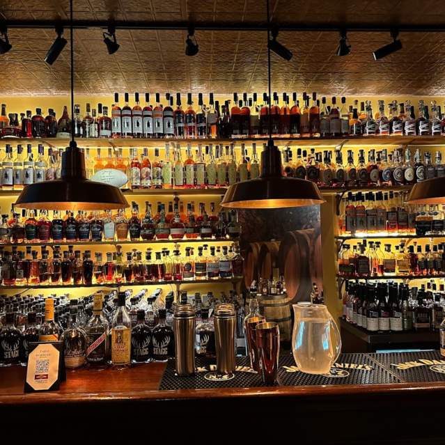 A backlit bar full of different bottles of bourbon
