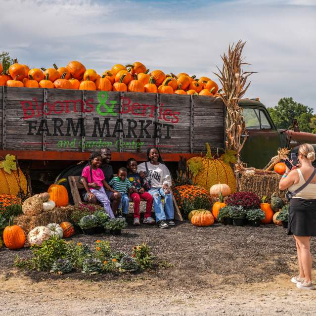 A group poses for a photo in front of a truck full of pumpkins at a fall festival