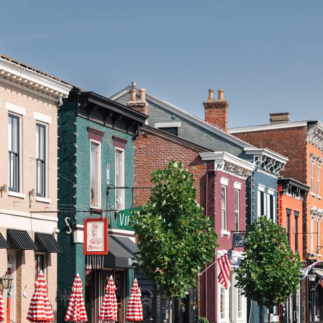 A line of buildings in various colors. There's trees and a grouping of red and white striped umbrellas.