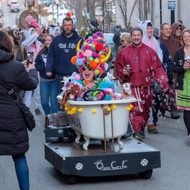 A woman sits in a bathtub during the Bockfest parade wearing a colorful pompom hat