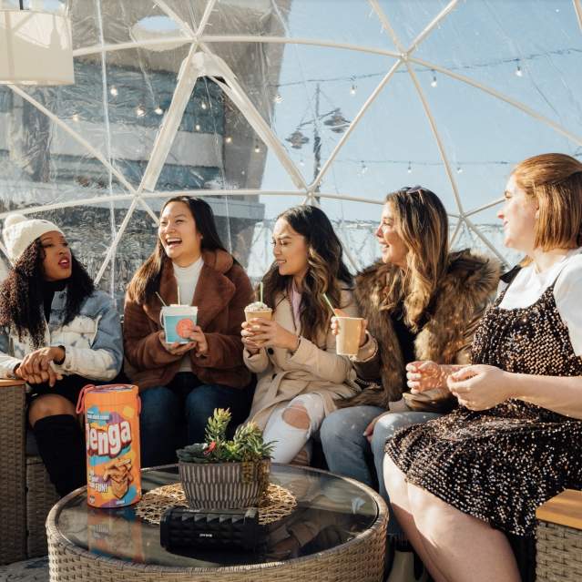 Image is of 5 women sitting in a clear igloo, laughing and having fun.