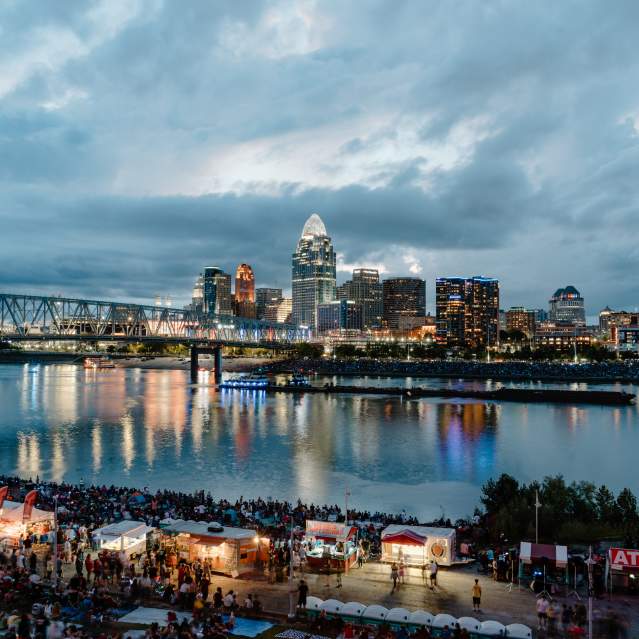Crowds of people gather along the river as the sun goes down.