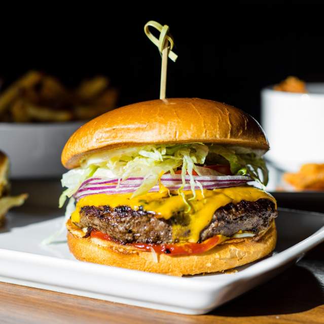 A classic cheeseburger on a bun with lettuce, red onion, and tomato. A pick goes through the bun holding it together.