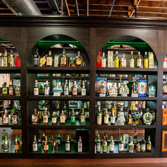A large 4 row shelf holds vintage spirits
