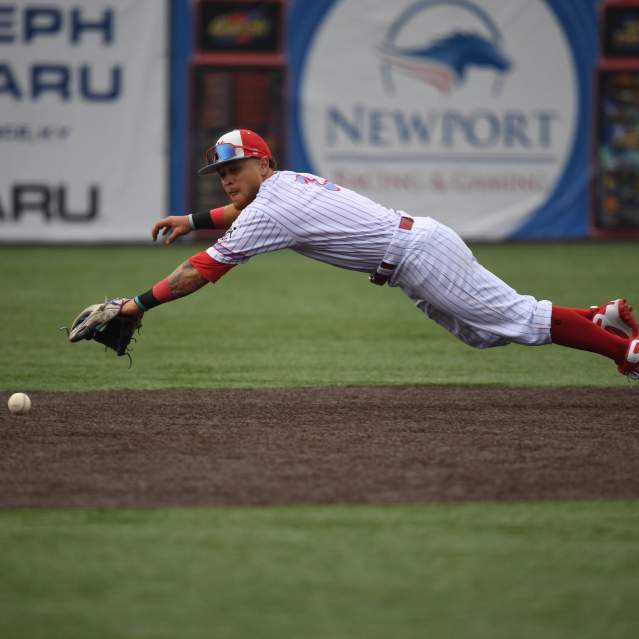 A baseball player is extended midair horizontally to catch a ball.