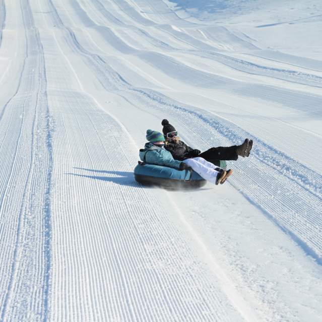 Image is on two people sharing a black inner tube sliding down a hill covered in snow.