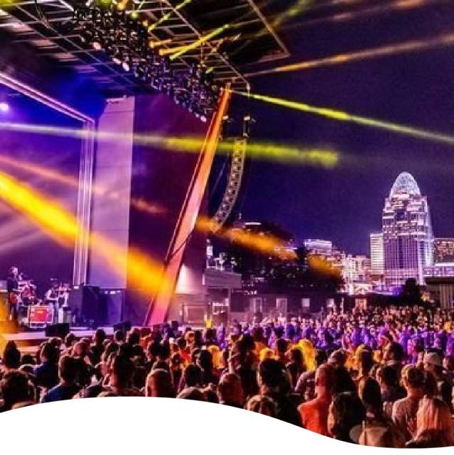 A crowd of people watching a band on a purple lighted stage. Streams of gold light reach out to the crowd.