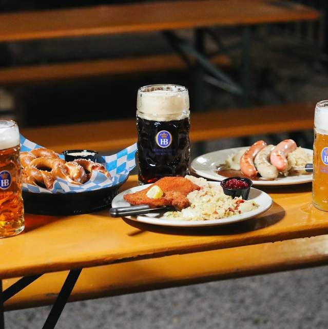 A bench laden with three steins of beer and plates of pretzels, schnitzel, and wursts at Hofbrauhaus in Newport, Ky.