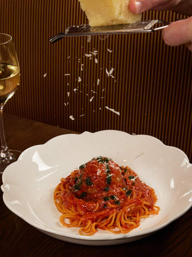 Fresh cheese is grated over a plate of pasta.