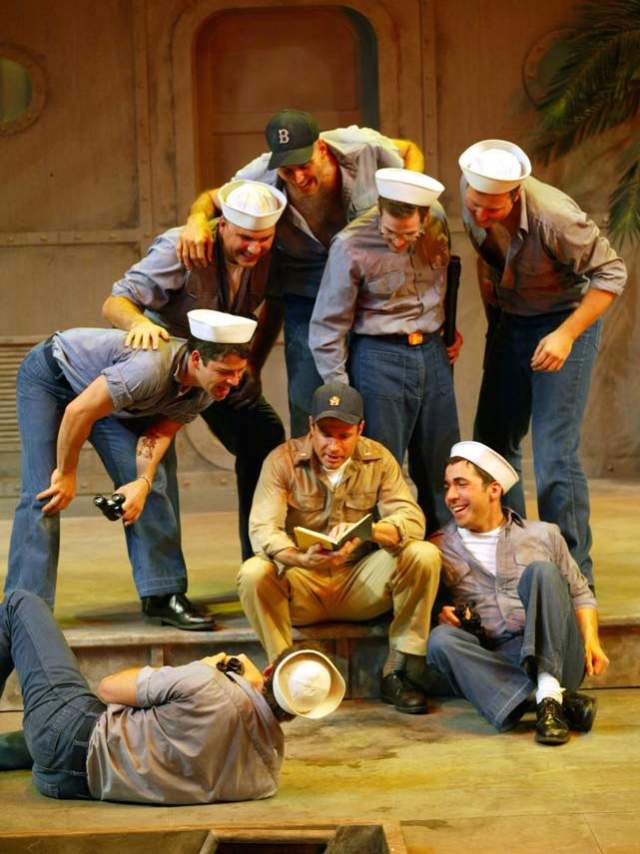 Image is of 8 men dressed in navy uniforms on a stage acting.
