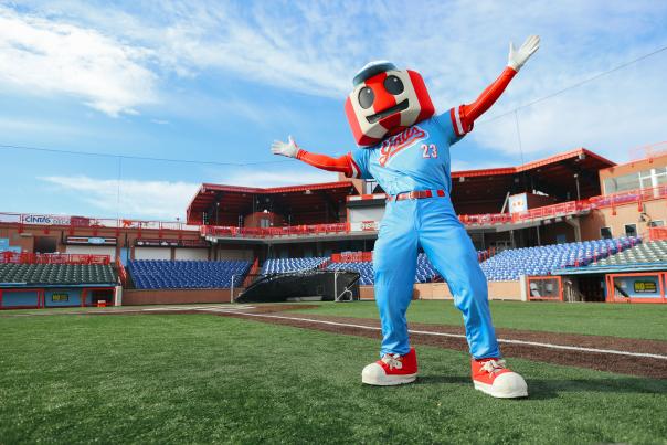 A red and white striped water tower mascot in a blue uniform stretches its arms wide with stadium seating behind.