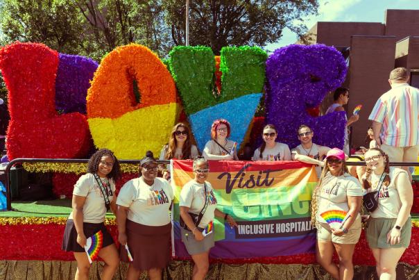 A group of Visit Cincy employees poses in front of a float for the Cincinnati Pride parade