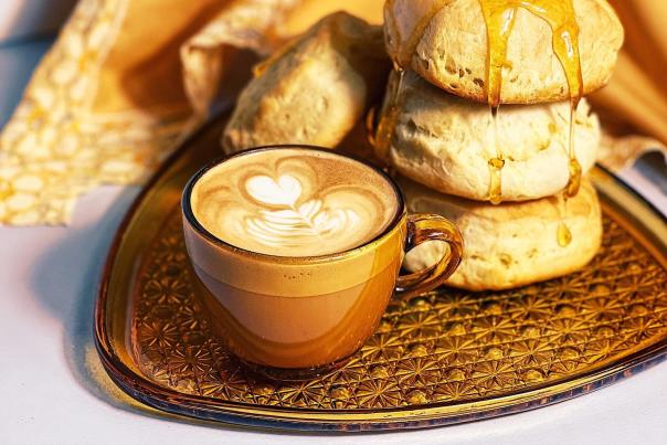 A golden-brown tray with three golden hued biscuits with honey drizzeled over it, sitting next to a brown and tan coffee mug with a late.