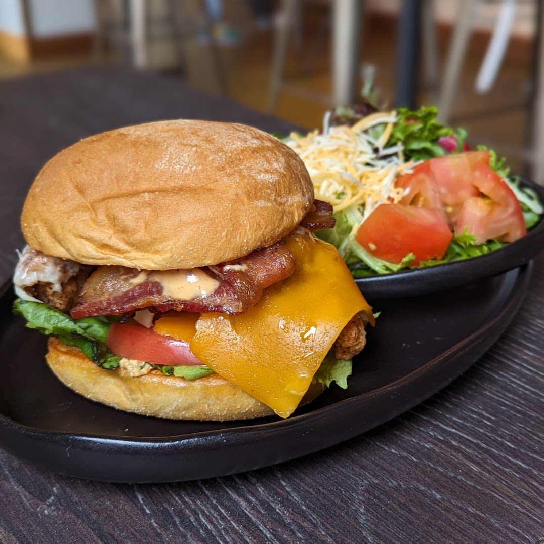 Image is of friend chicken sandwich with a side salad on a black plate.