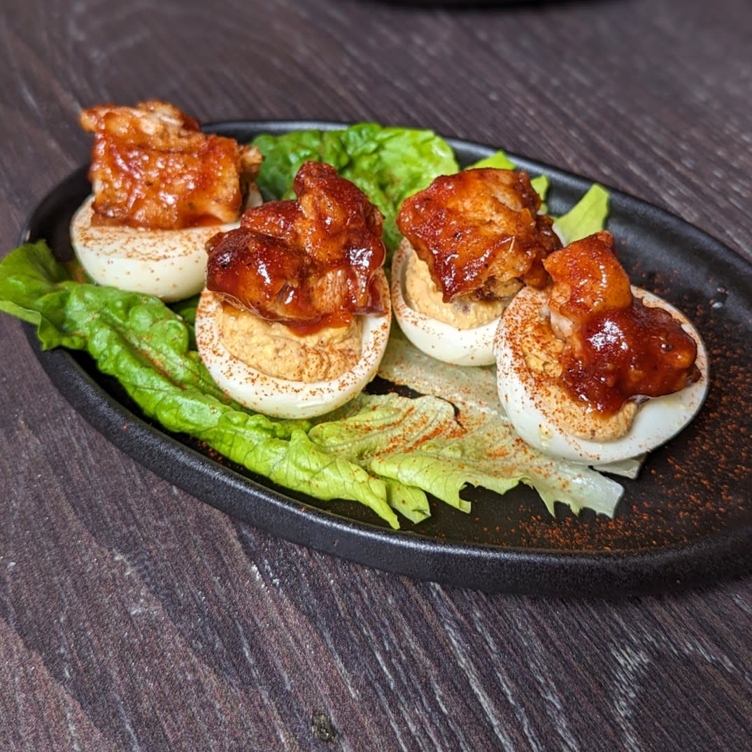 Image is of 4 deviled eggs with BBQ chicken on top on a black plate.