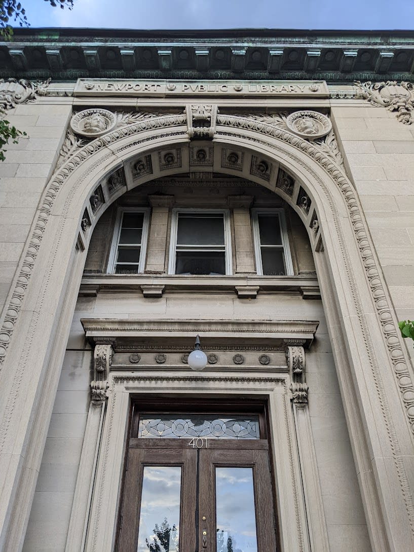 The image shows the front door and arch of the library with the words "Newport Public Library" above it.